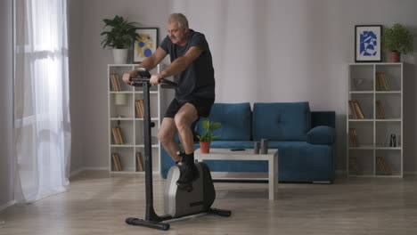 Fitness-En-Casa-Un-Hombre-De-Mediana-Edad-Está-Entrenando-En-Bicicleta-Estática-En-La-Sala-De-Estar-Ejercicio-Cardiovascular-Estilo-De-Vida-Saludable